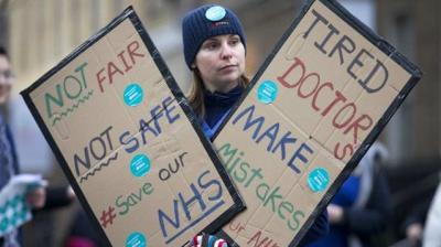 A junior doctor holds placards as they protest outside Guy's Hospital during a 24-hour strike over pay and conditions in London. (Photo:AFP)